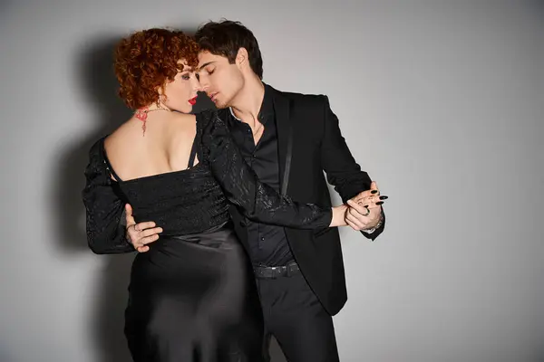 Beautiful sexy couple in black elegant attires kissing and hugging lovingly on gray background — Stock Photo