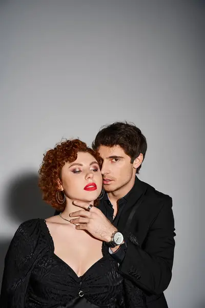 Appealing sexy couple in elegant black attires posing passionately together on gray background — Stock Photo