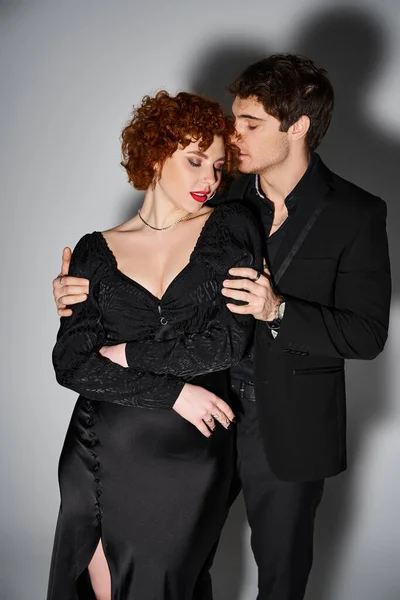 Atractivo novia y novio en debonair negro trajes abrazándose amorosamente en gris fondo - foto de stock