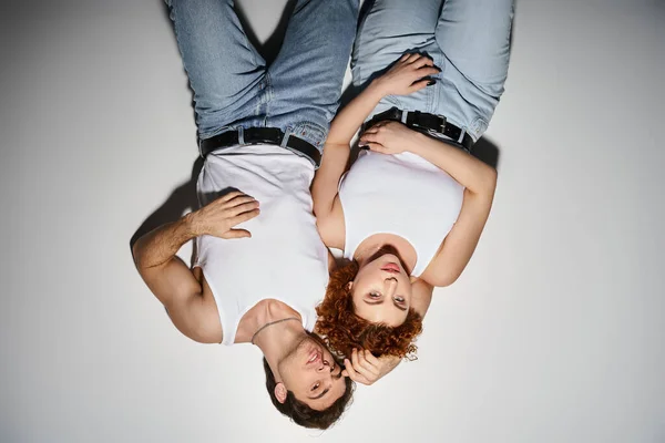 Atractivo hombre y mujer en pantalones vaqueros azules que yacen en el suelo juntos y mirando a la cámara, sexy pareja - foto de stock