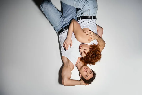 Homem bonito em jeans deitado no chão ao lado de sua jovem namorada e olhando para a câmera, casal sexy — Fotografia de Stock