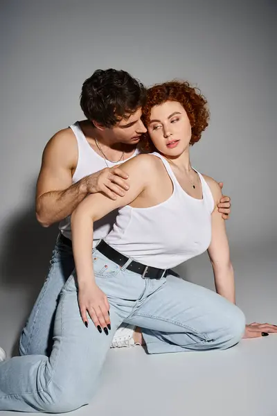 Charmanter Mann und Frau in blauen Jeans sitzen zusammen auf dem Boden und umarmen sich herzlich, sexy Paar — Stockfoto