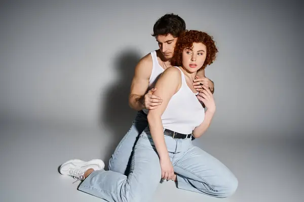 Соблазнительные мужчина и женщина в синих джинсах сидят на полу вместе и обнимаются теплой, сексуальной парой — стоковое фото