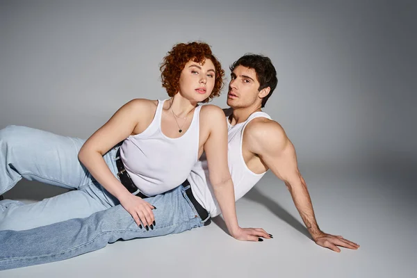Appealing sexy couple in comfy blue jeans reclining on floor together and looking at camera — Stock Photo