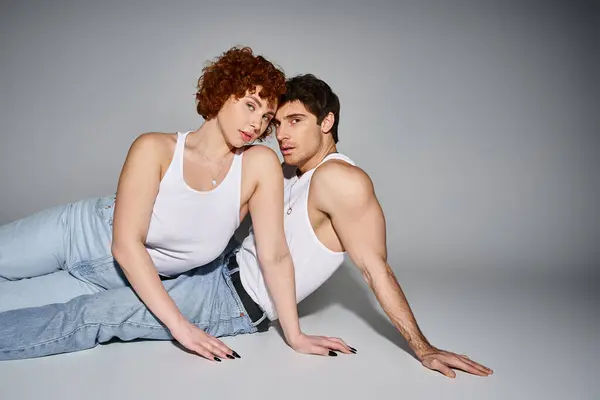 Atractivo sexy pareja en cómodo azul jeans reclinado en el suelo juntos y mirando a la cámara - foto de stock