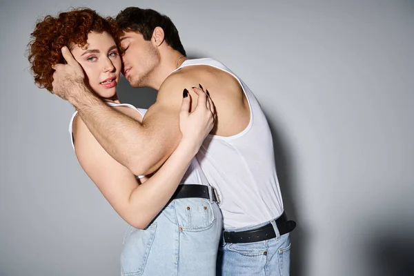 Schöne Frau in blauen Jeans, die in die Kamera schaut, während ihr Freund sie küsst, sexy Paar — Stockfoto
