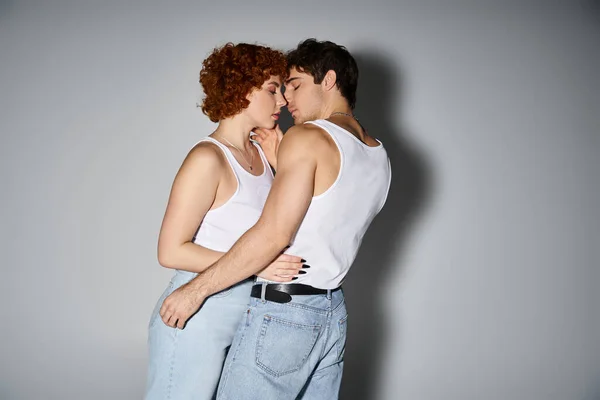 Attractive boyfriend and girlfriend in casual attire hugging lovingly on gray backdrop, sexy couple — Stock Photo