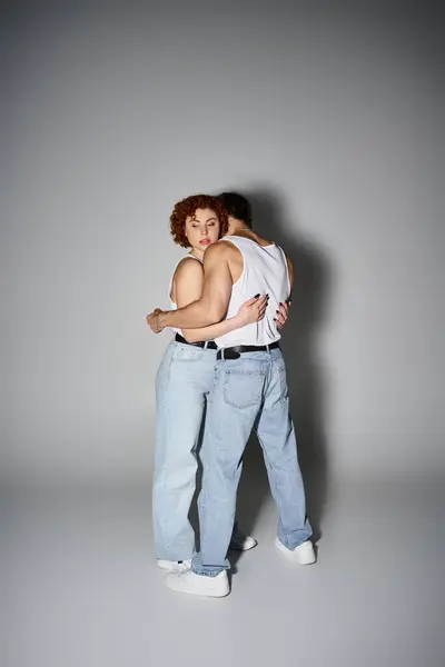 Appealing boyfriend and girlfriend in casual attire hugging lovingly on gray backdrop, sexy couple — Stock Photo