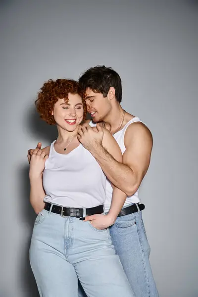 Cheerful boyfriend and girlfriend in casual attire hugging lovingly on gray backdrop, sexy couple — Stock Photo