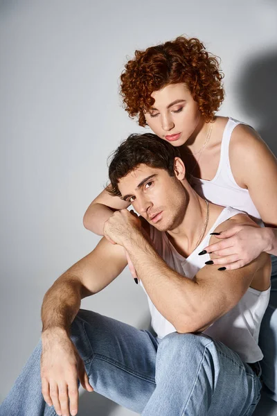 Bonita mujer sentada en el suelo y abrazando a su novio guapo que mira a la cámara, sexy pareja - foto de stock
