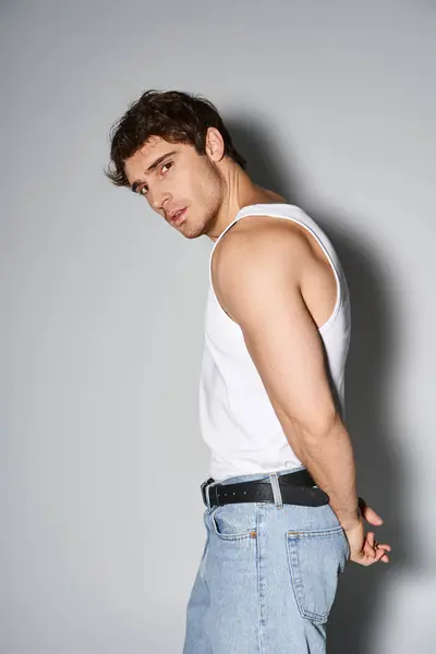 Good looking alluring man in blue casual jeans standing on gray backdrop and looking at camera — Stock Photo