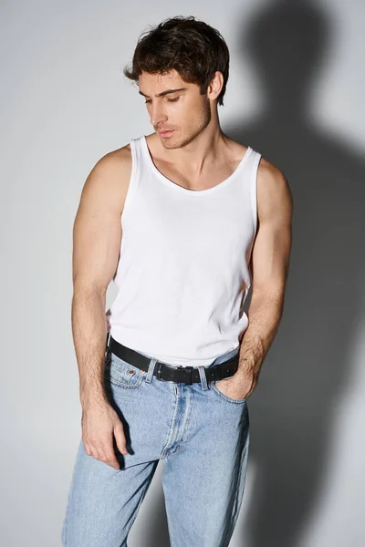 Handsome sexy man in casual blue jeans with black belt standing and posing on gray backdrop — стоковое фото