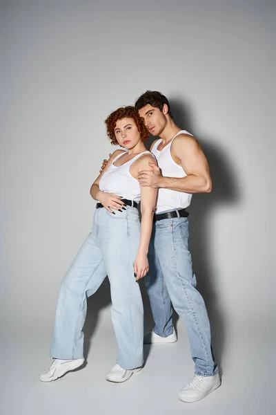 Заманчивые мужчина и женщина в случайных синих джинсах обнимаются тепло и смотрят в камеру, сексуальная пара — стоковое фото