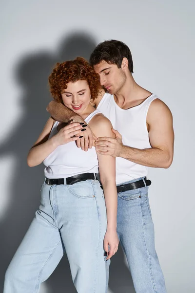 Alegre seductor hombre y mujer en jeans posando sobre gris telón de fondo y sonriendo felizmente, sexy pareja - foto de stock