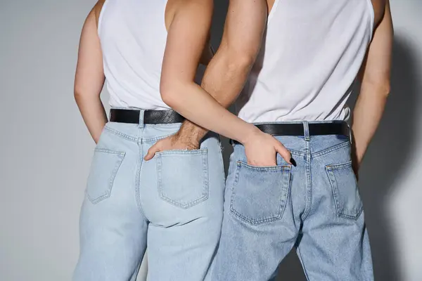 Vista posterior de hombre y mujer cariñosos en vaqueros azules casuales posando con las manos en los bolsillos, sexy pareja - foto de stock