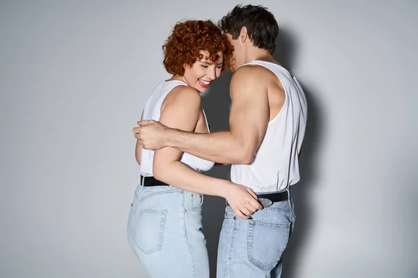 Fröhlich verführerisch Mann und Frau in Jeans posieren vor grauem Hintergrund und lächeln glücklich, sexy Paar — Stockfoto