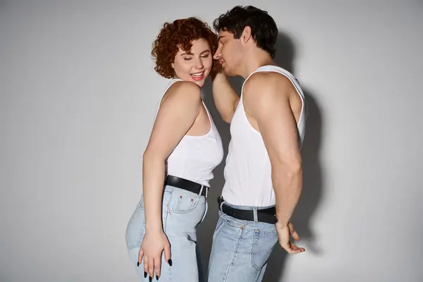 Cheerful alluring man and woman in jeans posing on gray backdrop and smiling happily, sexy couple — Stock Photo