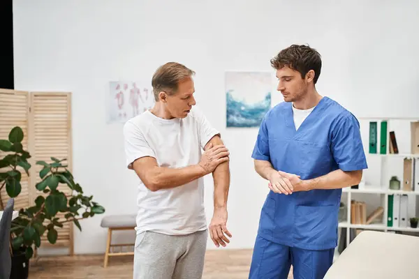 Schöner engagierter Arzt in blauer Uniform, der seinem reifen Patienten beim Termin zuhört — Stockfoto