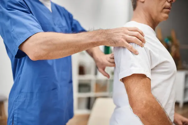 Visão recortada de médico dedicado em roupão azul ajudando seu paciente maduro a se reabilitar na enfermaria — Fotografia de Stock