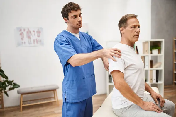 Gut aussehender Arzt in medizinischer Robe bei der Rehabilitation seiner reiferen gutaussehenden Patientin auf der Krankenhausstation — Stockfoto