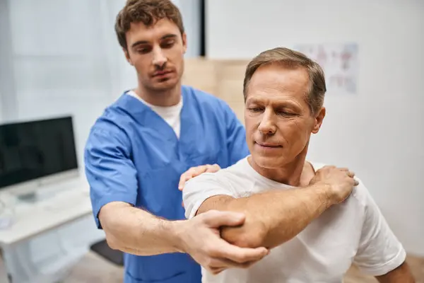 Gut aussehender Patient in lässiger Kleidung, der seine Muskeln mit Hilfe seines gutaussehenden Arztes dehnt — Stockfoto