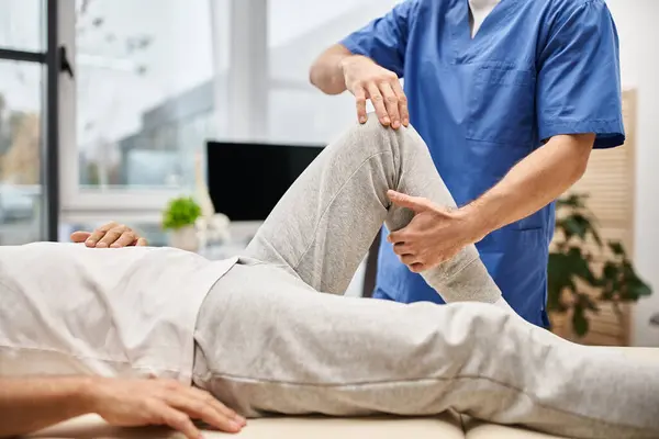 Ausgeschnittene Ansicht eines engagierten Arztes in blauer Robe, der die Muskeln seines reifen Patienten im Krankenhaus dehnt — Stockfoto