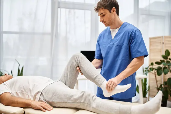Attractive devoted doctor rehabilitating muscles of his mature patient on appointment in hospital — Stock Photo