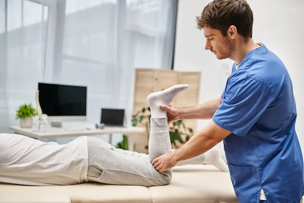 Handsome dedicated doctor rehabilitating muscles of his mature patient on appointment in hospital — Stock Photo