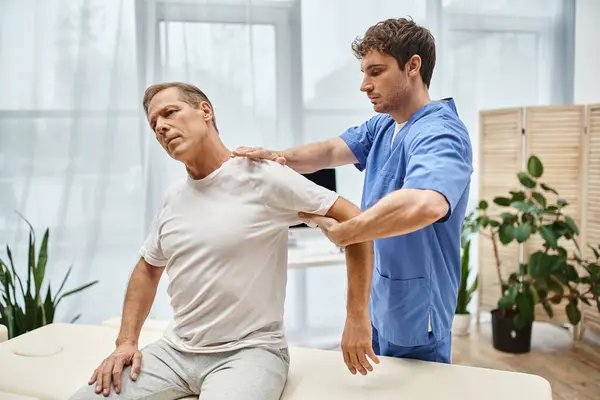 Good looking mature patient during appointment with his handsome rehabilitologist in hospital ward — Stock Photo