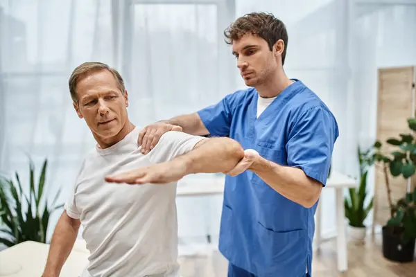 Attractive mature patient in cozy attire on appointment with his rehabilitologist in hospital ward — Stock Photo