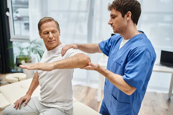 Good looking mature patient sitting during appointment with his rehabilitologist in hospital ward — Stock Photo
