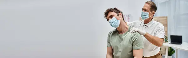 Médico maduro atraente com máscara ajudando seu paciente a se reabilitar na enfermaria do hospital, bandeira — Fotografia de Stock