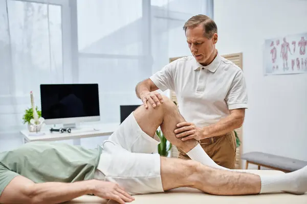 Good looking mature doctor checking up knees of his patient in hospital, rehabilitation concept — Stock Photo