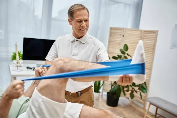 Beau médecin mature vérifiant les genoux de son patient à l'hôpital, concept de réadaptation — Photo de stock