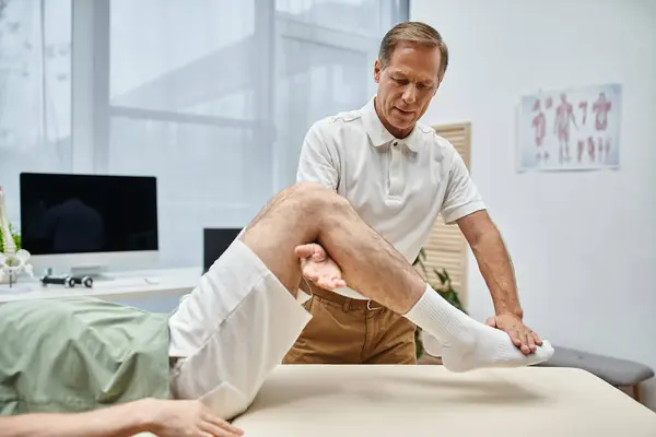 Buen aspecto médico maduro comprobar las rodillas de su paciente en el hospital, concepto de rehabilitación - foto de stock