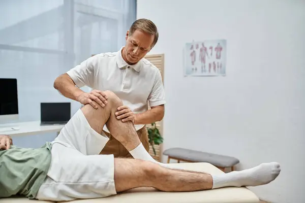 Good looking mature doctor checking up knees of his patient in hospital, rehabilitation concept — Stock Photo