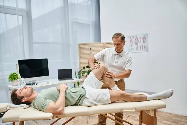 Beau médecin mature vérifiant les genoux de son patient à l'hôpital, concept de réadaptation — Photo de stock