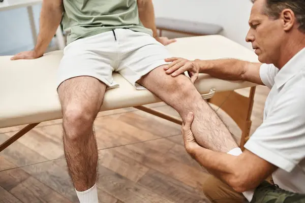 Gut aussehender, reifer Arzt untersucht Knie seines Patienten im Krankenhaus, Rehabilitationskonzept — Stockfoto