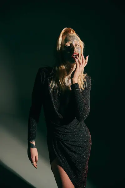 Tattooed blonde woman with glitter on face and red lips posing in shiny dress on black backdrop — Stock Photo