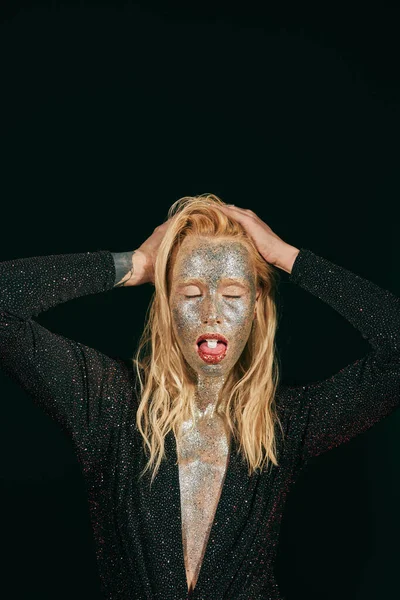 Jeune femme blonde avec maquillage paillettes et les yeux fermés montrant la langue avec pilule sur fond noir — Photo de stock