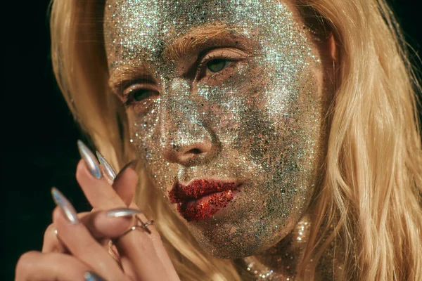 Close up of blonde woman with green eyes and glitter on face and body posing on black backdrop — Stock Photo