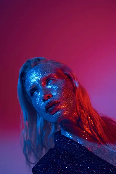 Blonde and shiny woman with glitter on face and sparkling outfit posing on vibrant neon background — Stock Photo