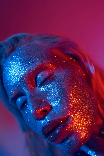 Nahaufnahme einer jungen und glänzenden Frau mit funkelndem Glitzern im Gesicht, die auf lebendigem Neon-Hintergrund posiert — Stockfoto