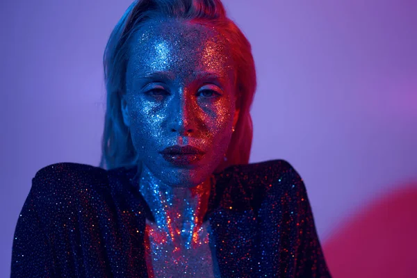Portrait de modèle étincelant recouvert de paillettes posant en tenue brillante sous des lumières colorées en studio — Photo de stock