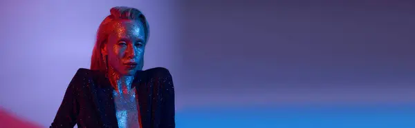 Banner of alluring woman covered in glitter posing in shiny outfit under colored lights in studio — Stock Photo