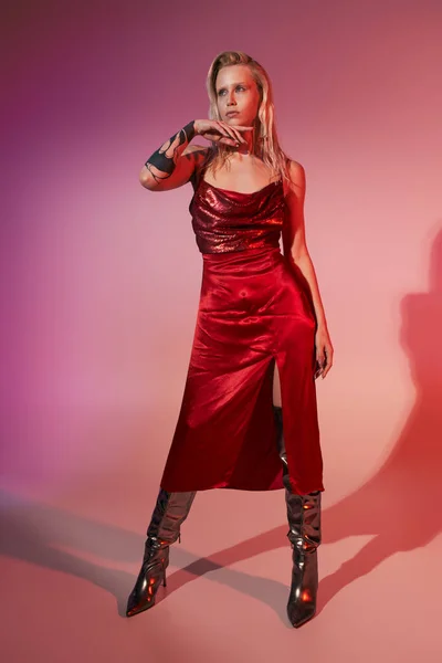Attractive fashionista model wearing red stylish dress and posing on pink backdrop, looking away — Stock Photo