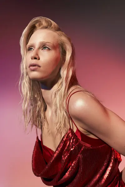 Приваблива молода жінка в червоній сексуальній сукні з довгим світлим волоссям, що дивиться на рожевий фон — стокове фото