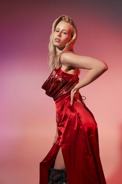 Mulher elegante atraente com cabelos longos em vestido vermelho com as mãos nos quadris e olhando para a câmera — Fotografia de Stock