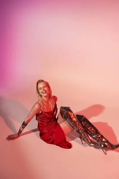 Cheerful beautiful woman in red fashionable dress sitting on floor and looking away joyfully — Stock Photo