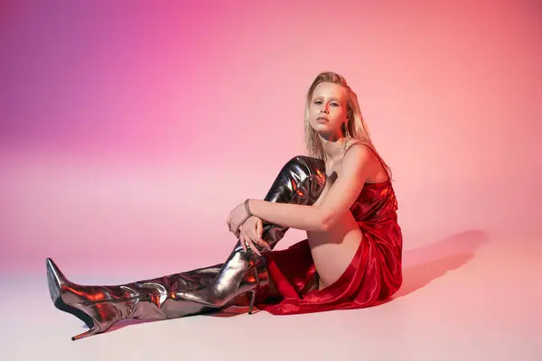 Verführerisch modisches weibliches Modell in rotem schickem Kleid auf dem Boden sitzend und direkt in die Kamera blickend — Stockfoto